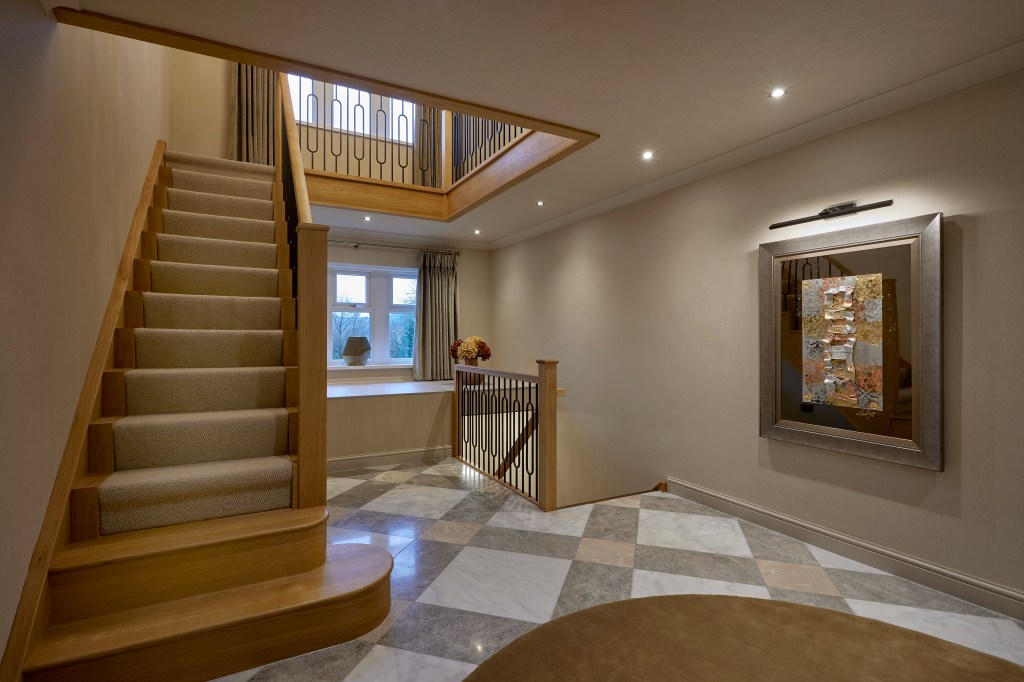 Modern hallway landing in Denshaw featuring a checkered marble floor, custom wall art with picture lighting, and an oak staircase.