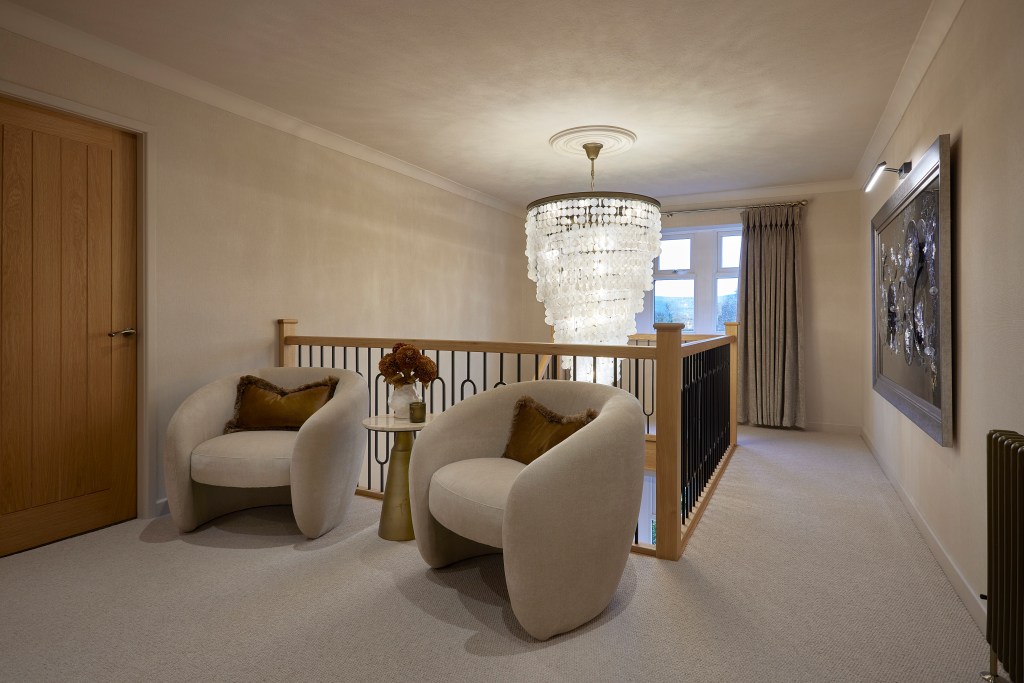 A luxury landing lounge in Denshaw featuring two curved velvet armchairs with rust cushions, a capiz shell chandelier, and a custom oak banister.