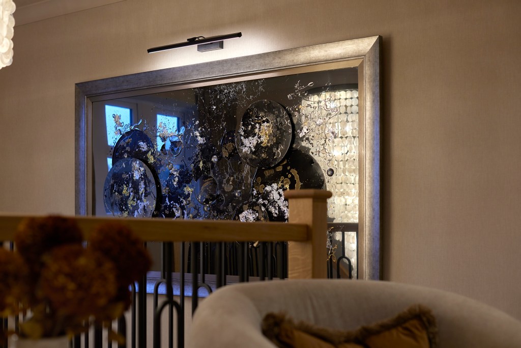 A grand landing in a Denshaw home featuring an oversized capiz shell chandelier, a large silver-framed abstract painting, and neutral velvet armchairs.