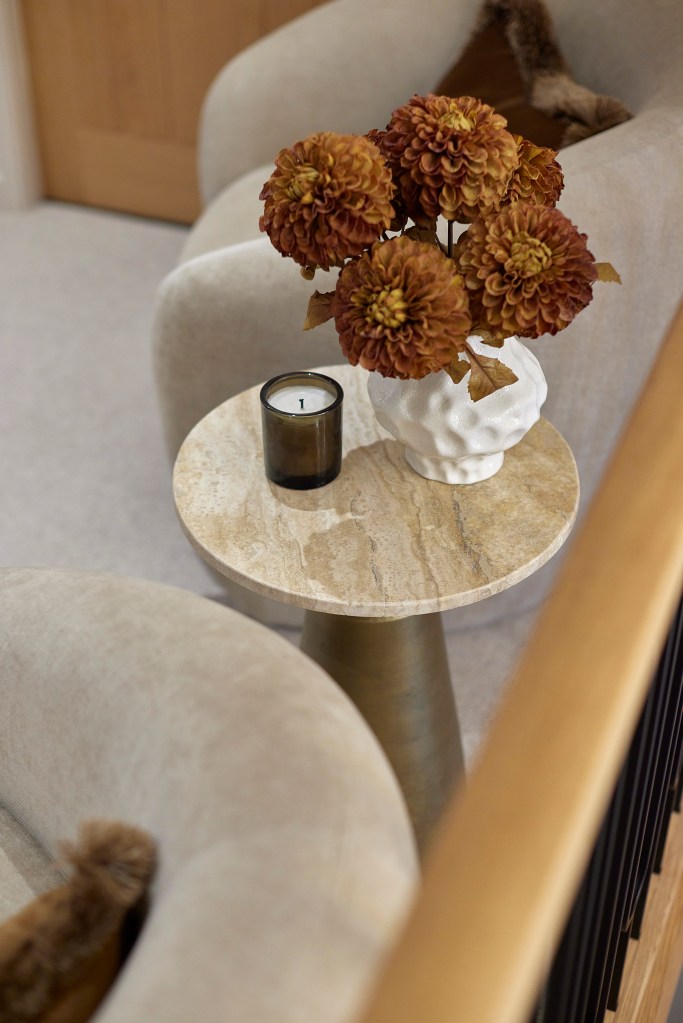 A small round travertine side table with a white textured vase of rust-colored flowers and a candle on a landing.