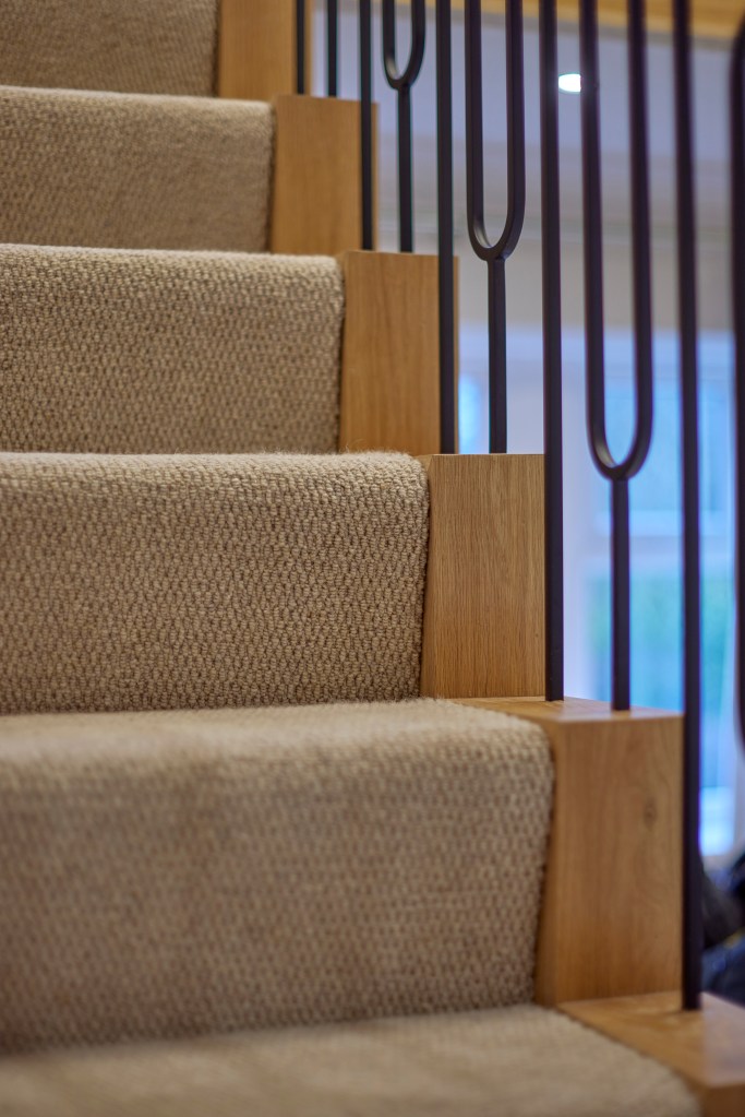 Close-up of neutral loop-pile stair carpet on an oak staircase with black iron balustrade spindles.