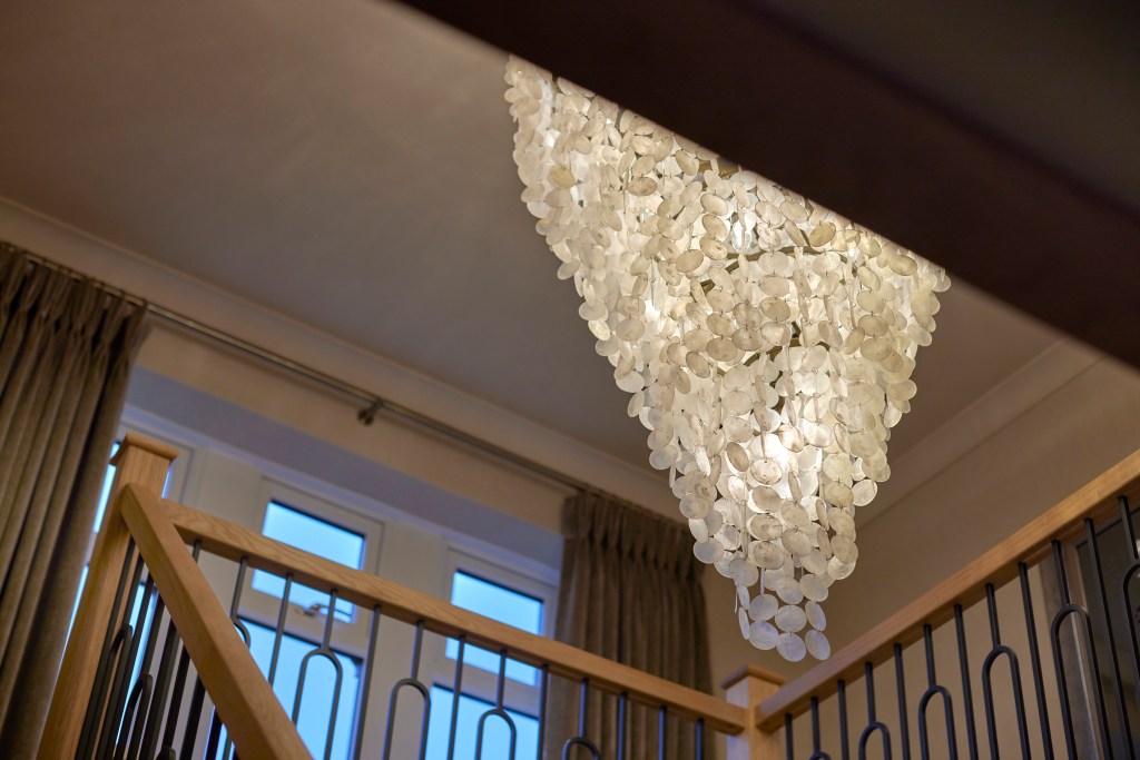 Vertical view of an oak staircase with iron balustrades and a large capiz shell chandelier in a Denshaw home.