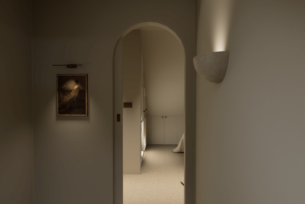A bright cottage staircase in Saddleworth with white spindles, an oak handrail, and a neutral wool stair runner leading to an arched doorway.