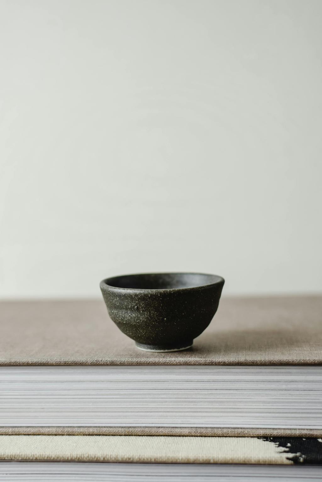 High-contrast close-up of three hand-thrown ceramic bowls of varying sizes, all glazed in matte white. The slightly uneven, wobbly rims and subtle fingerprints in the clay are emphasized by studio lighting, symbolizing commodified imperfection.